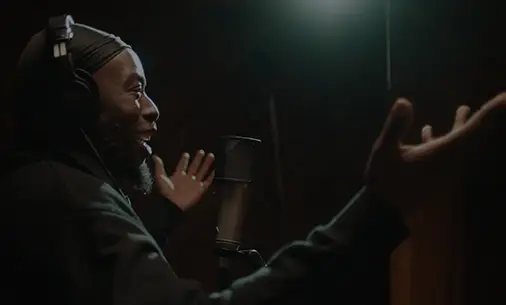 Preview image of video thumbnail showing an HS patient in a black hoodie with over the ear headphone standing in front of a microphone. 